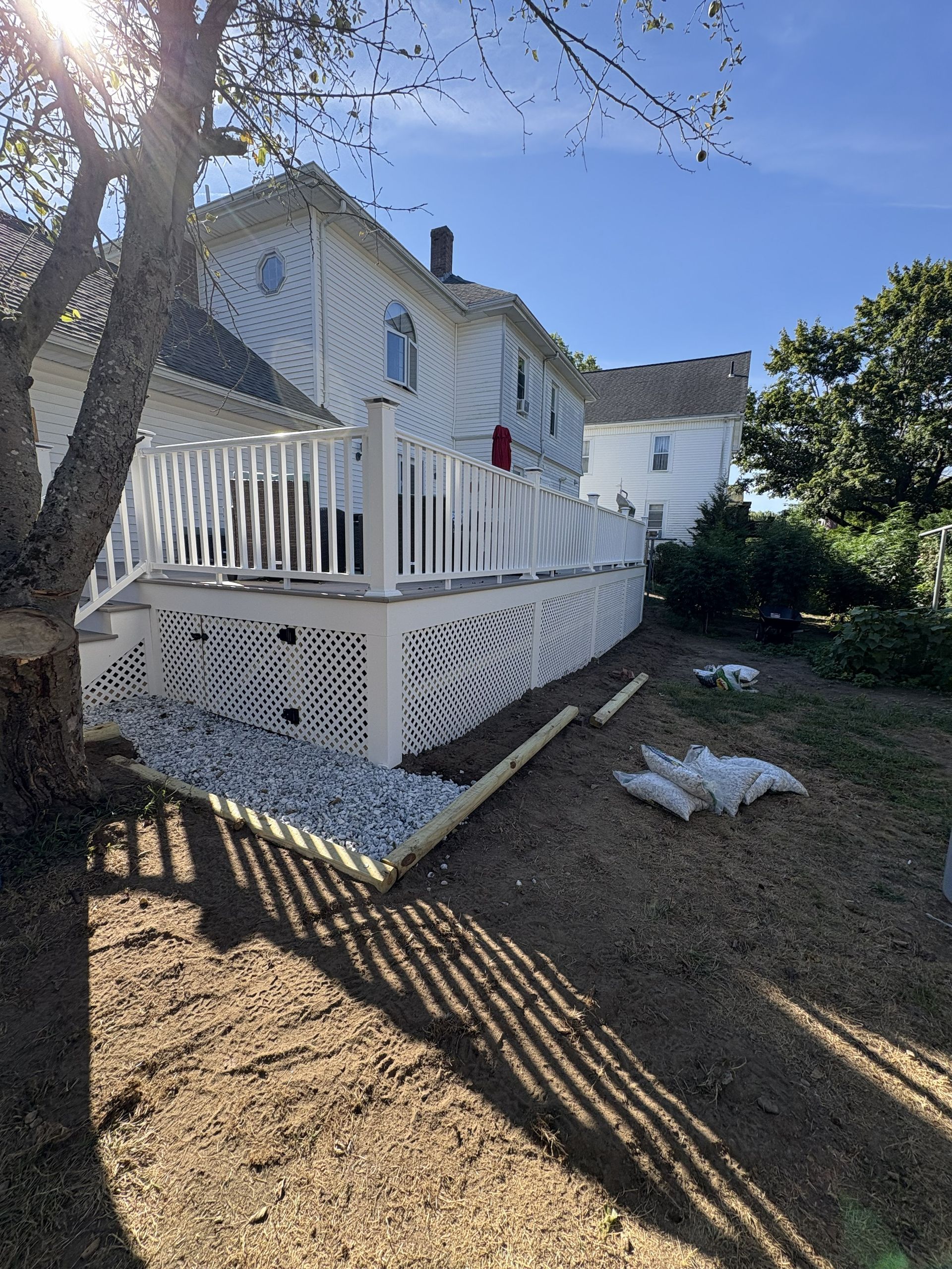 White house with porch and lattice skirting in a sunny yard, viewed from the side.
