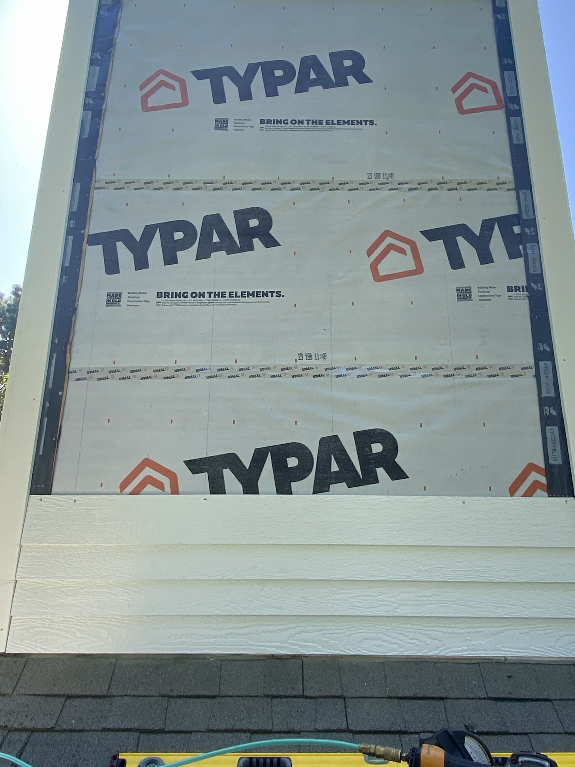 Partially built house exterior with Typar house wrap and exposed framing under a blue sky