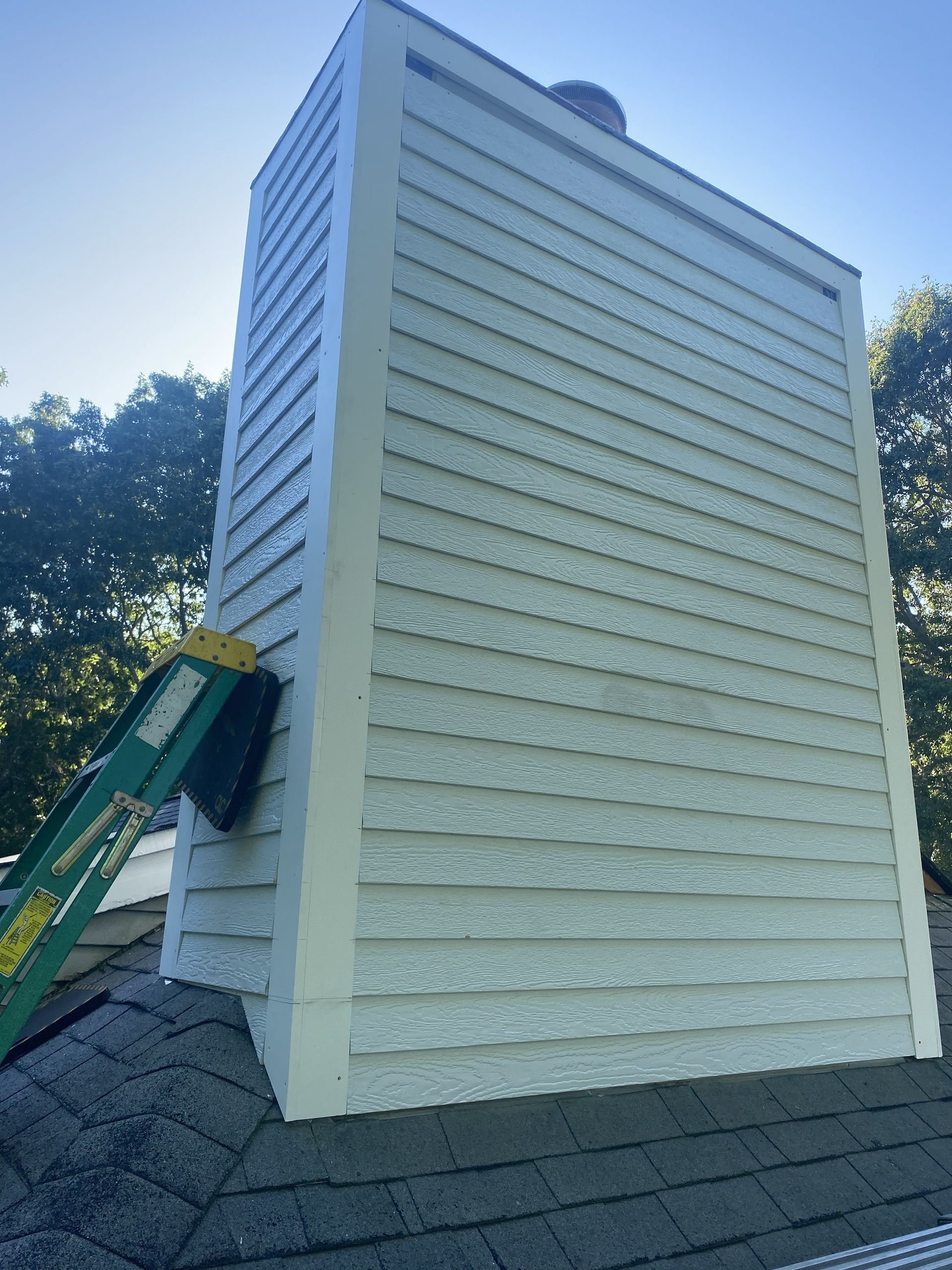 White rooftop vent shaft with louvered sides and a green ladder against it under a blue sky