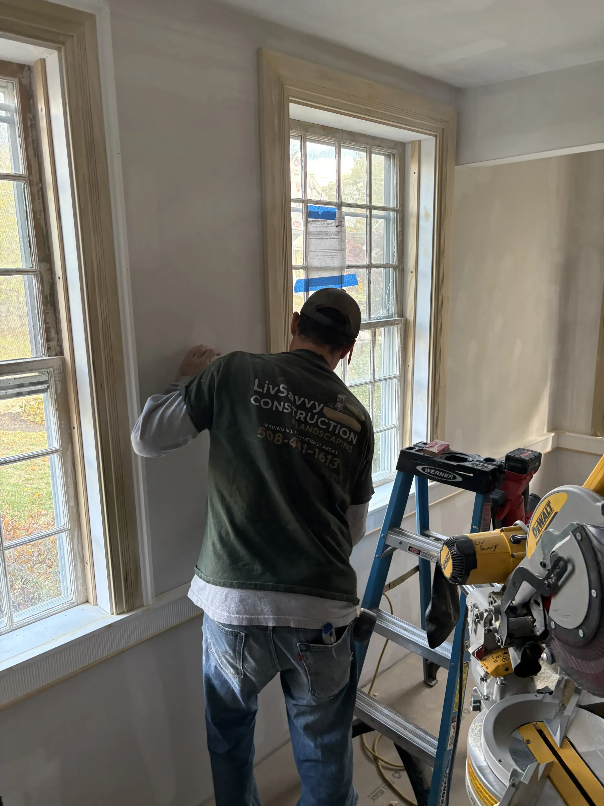 Worker painting a room near windows beside a miter saw and other tools