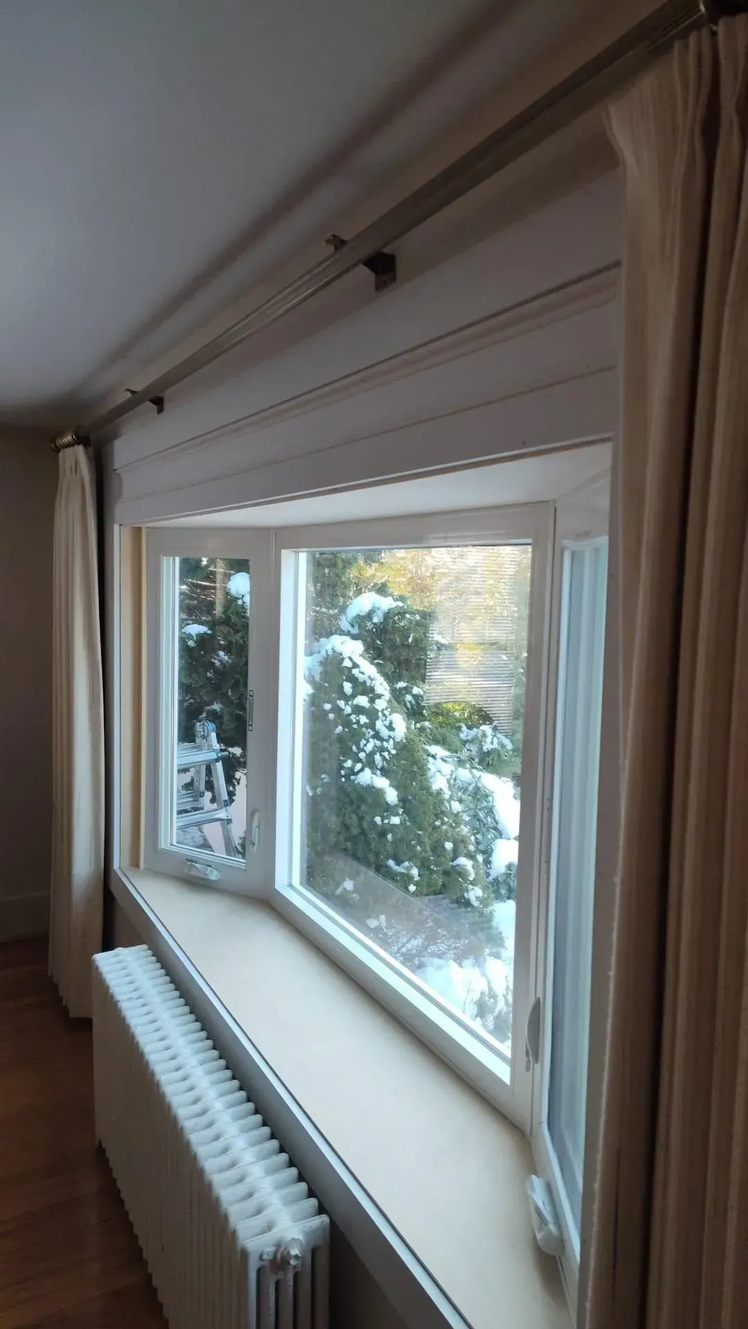 Bright living room window with cream curtains and a white radiator overlooking snowy trees outside