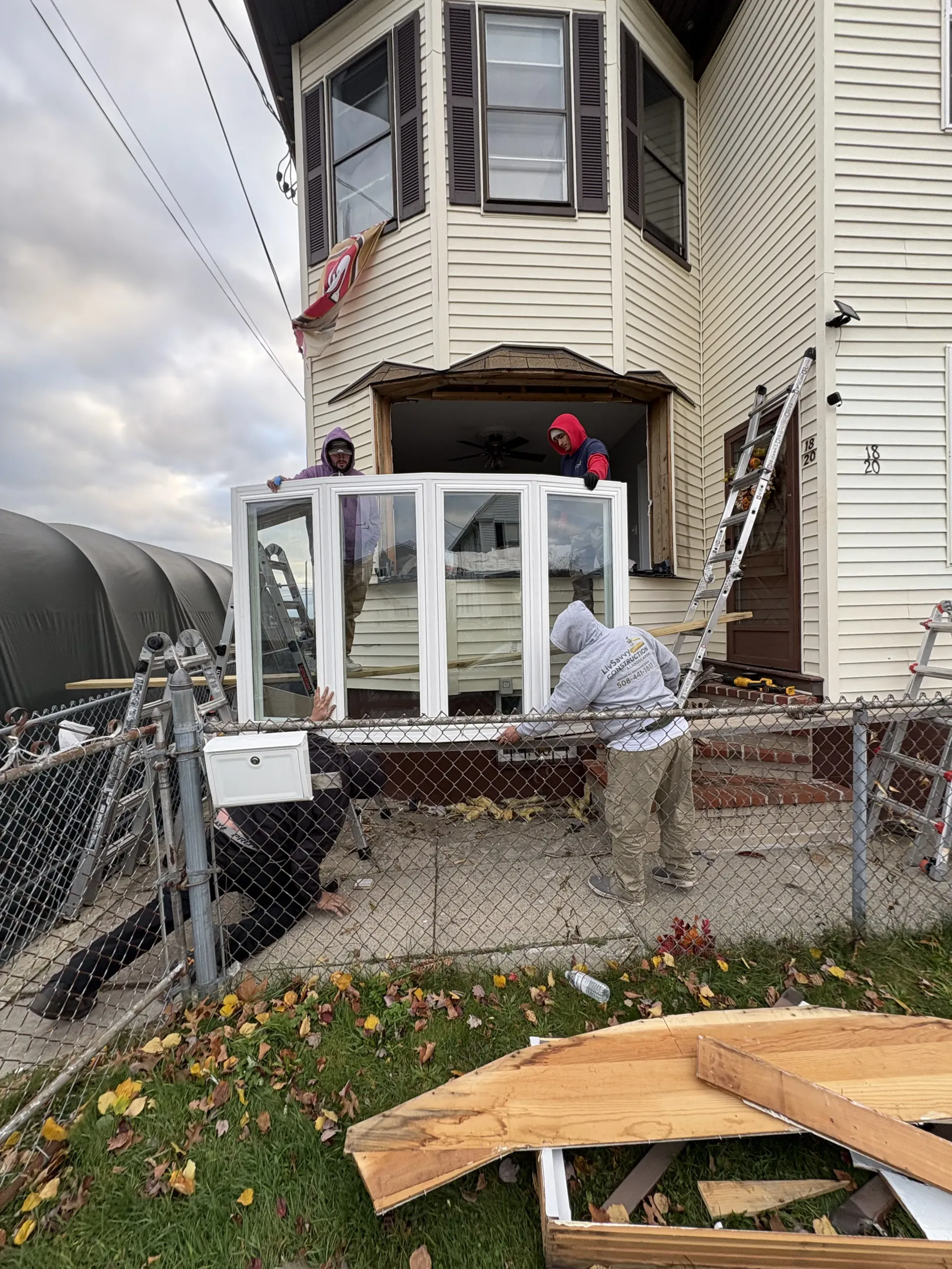 Damaged front porch of a house with broken railing, shattered glass, and debris by a chain-link fence