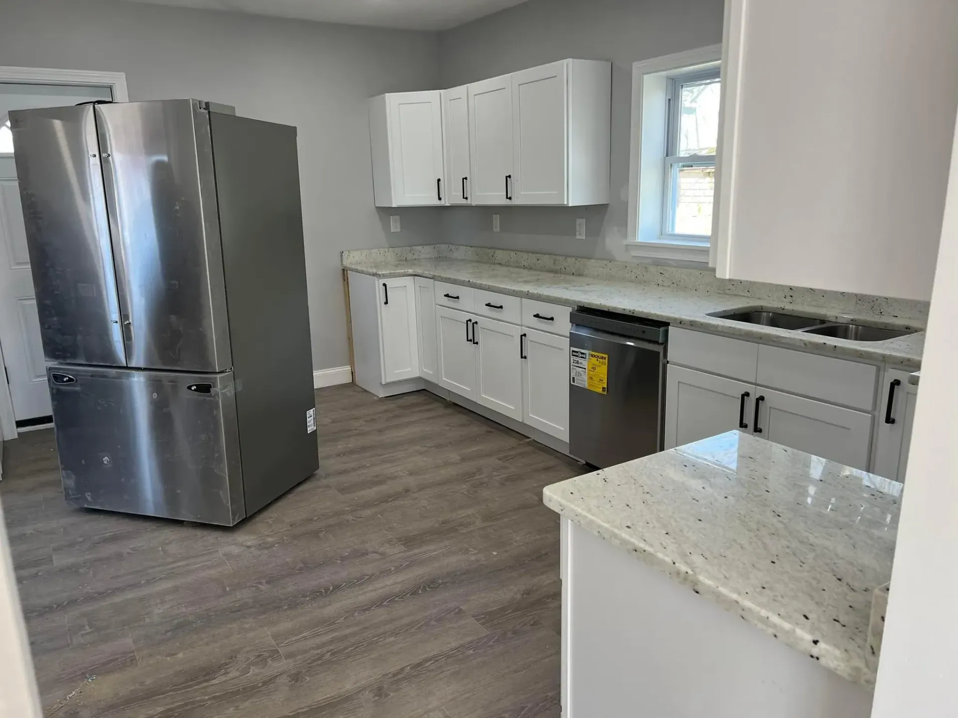 Modern kitchen with stainless steel fridge, white cabinets, gray counters, and wood-look flooring