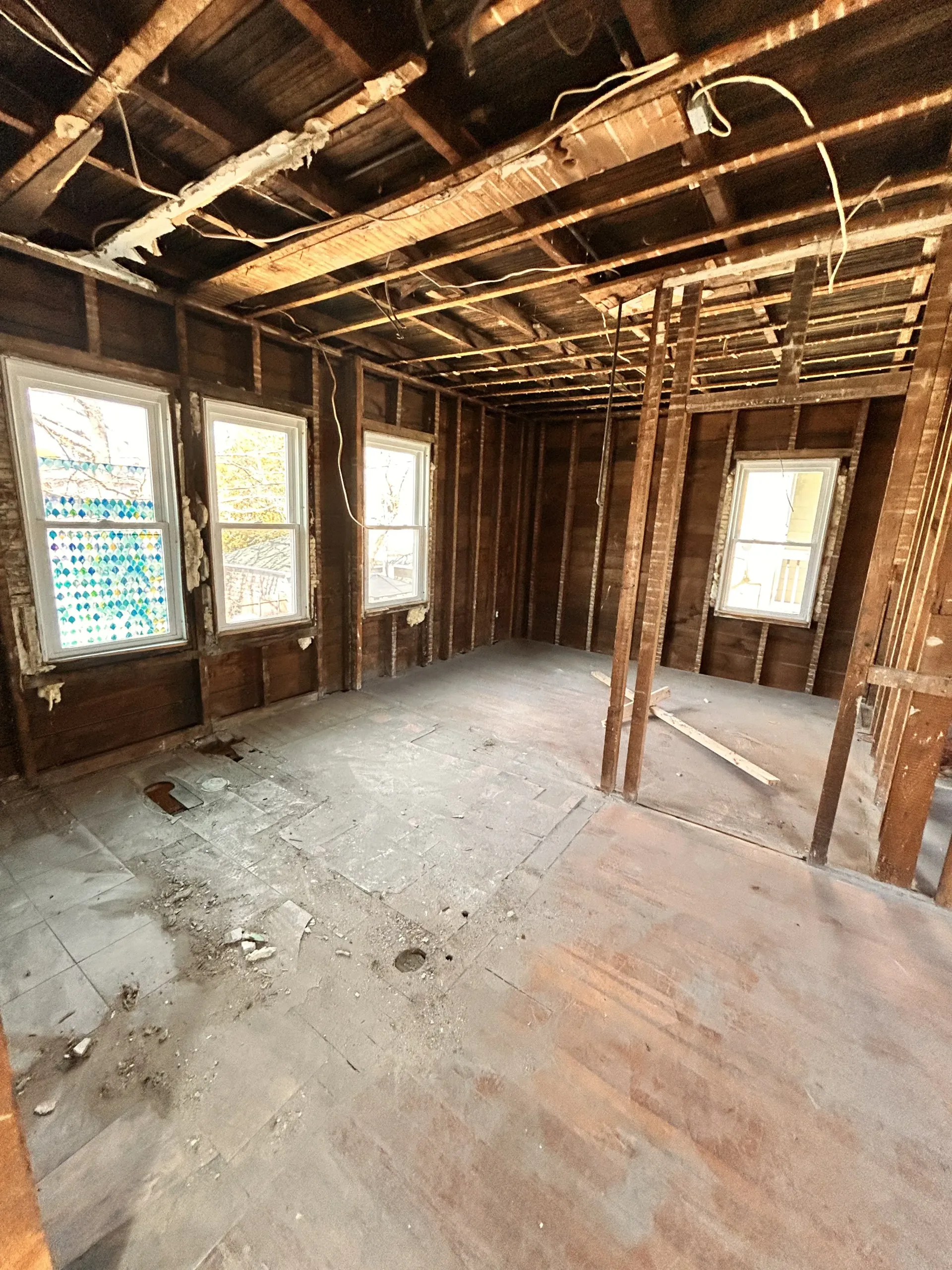 Exposed interior of a house under renovation, with unfinished wood framing, windows, and bare subfloor.