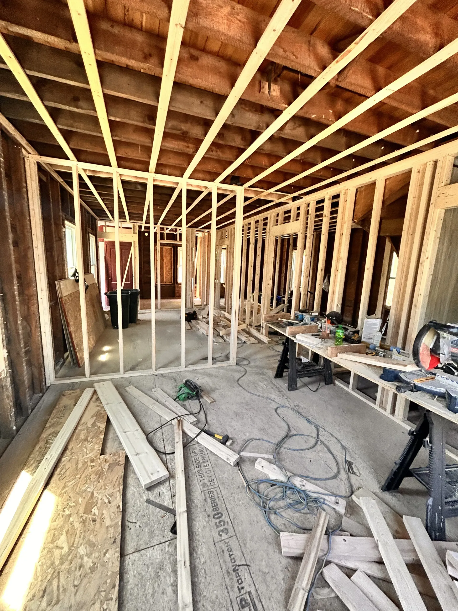 Framed interior of a house under construction with exposed studs, tools, and lumber on the floor.