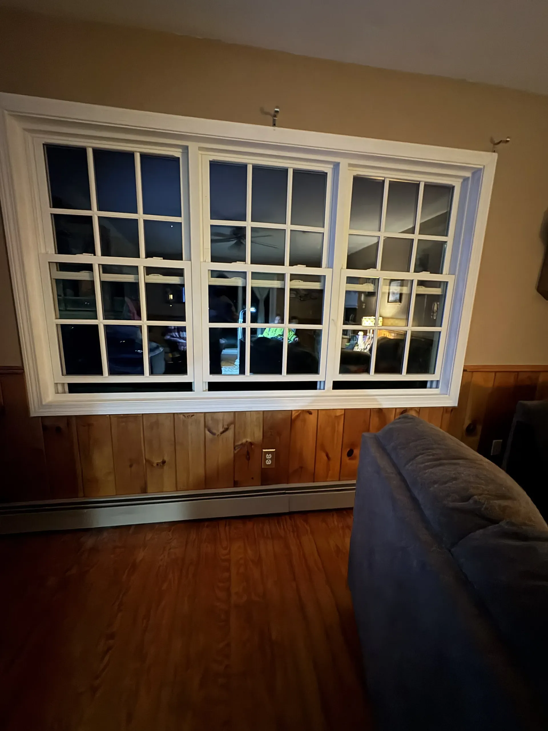 Living room with a large white-framed window, hardwood floors, and part of a couch in the foreground
