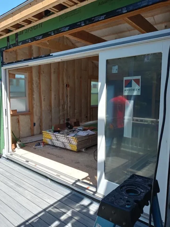 Open sliding glass doors to a wood-framed room under construction with materials on the floor