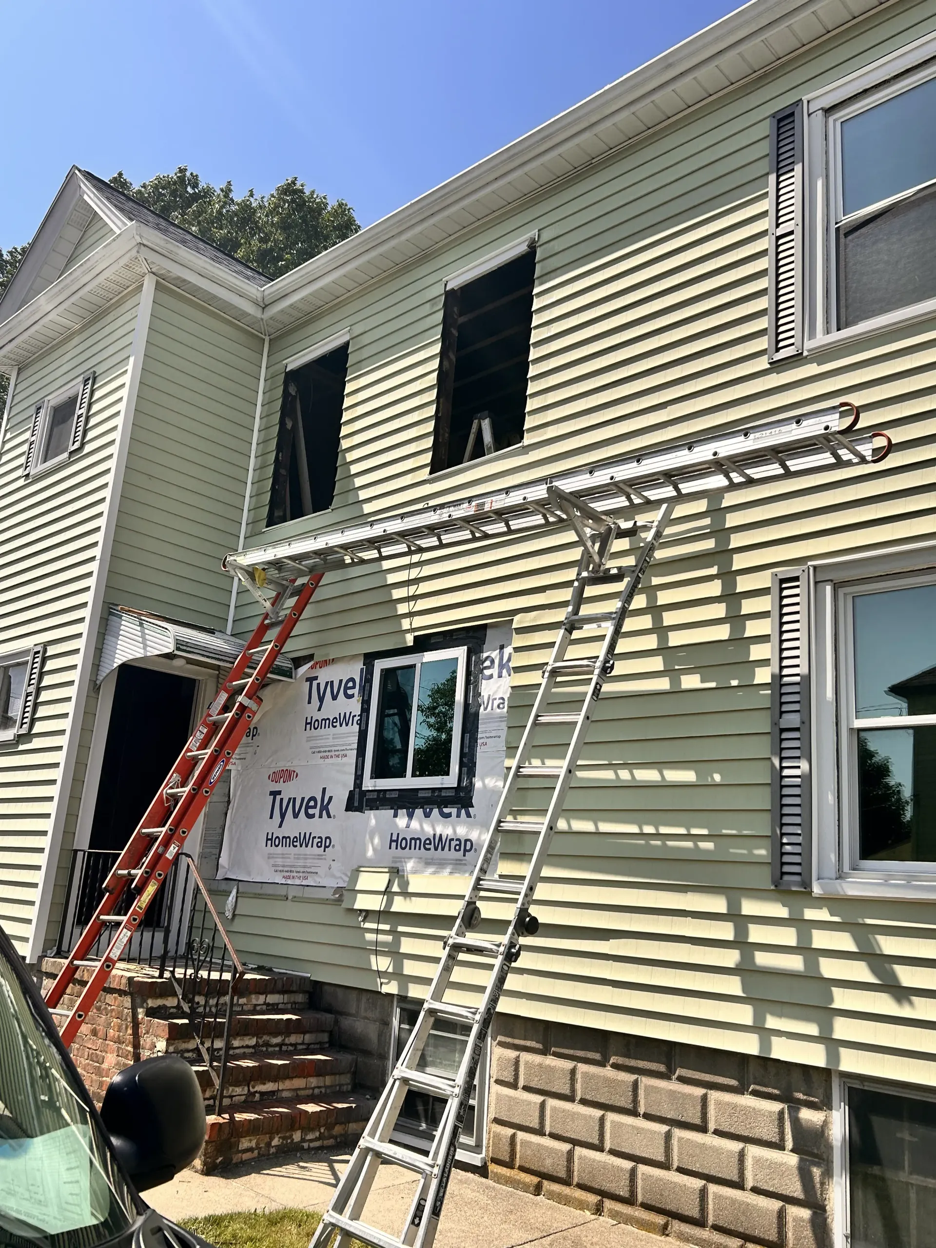 Ladders leaning against a house with workers' tools and scaffolding under exterior siding repair