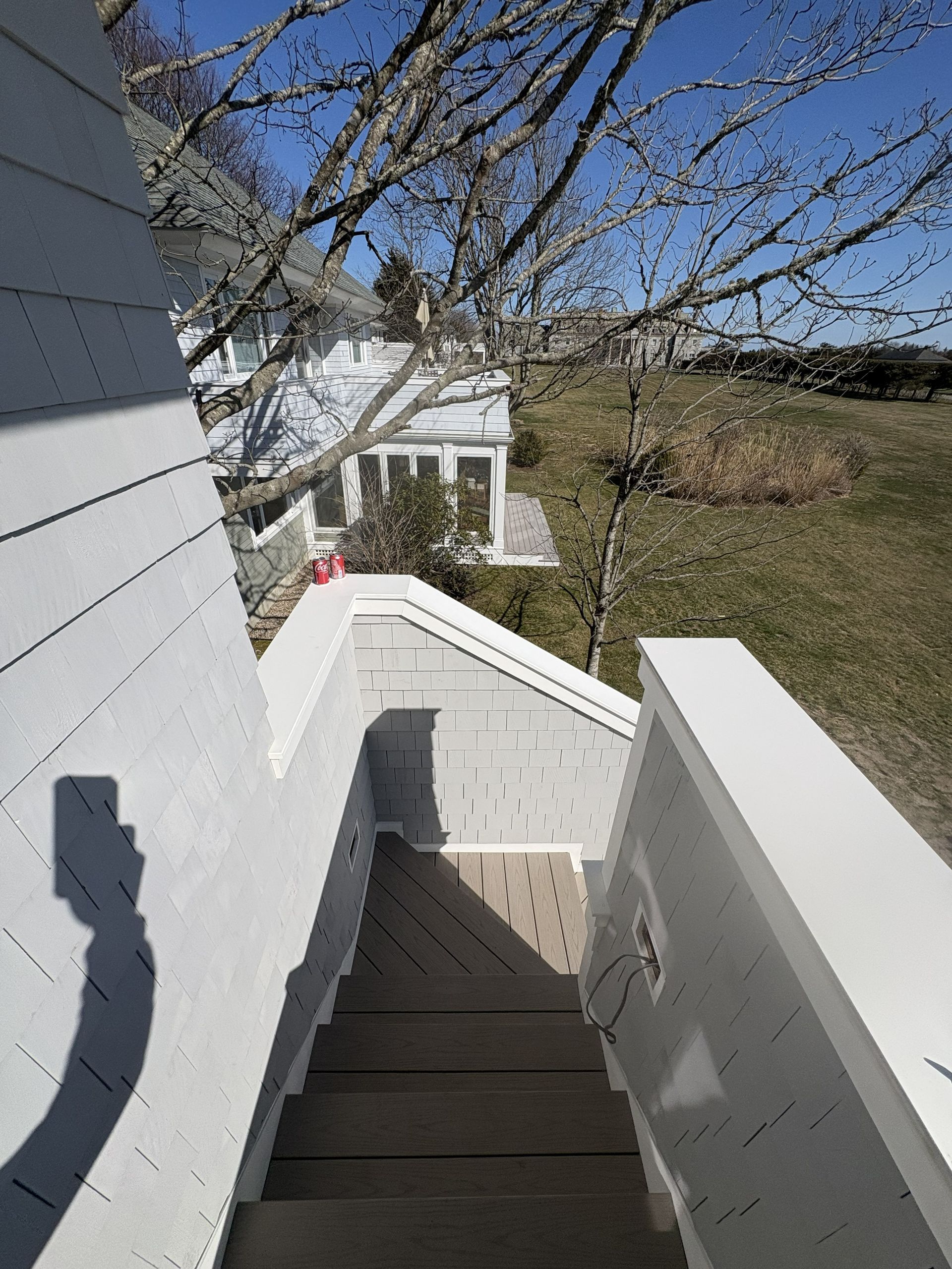 Outdoor stairway beside a white house, descending to a grassy yard on a sunny day.