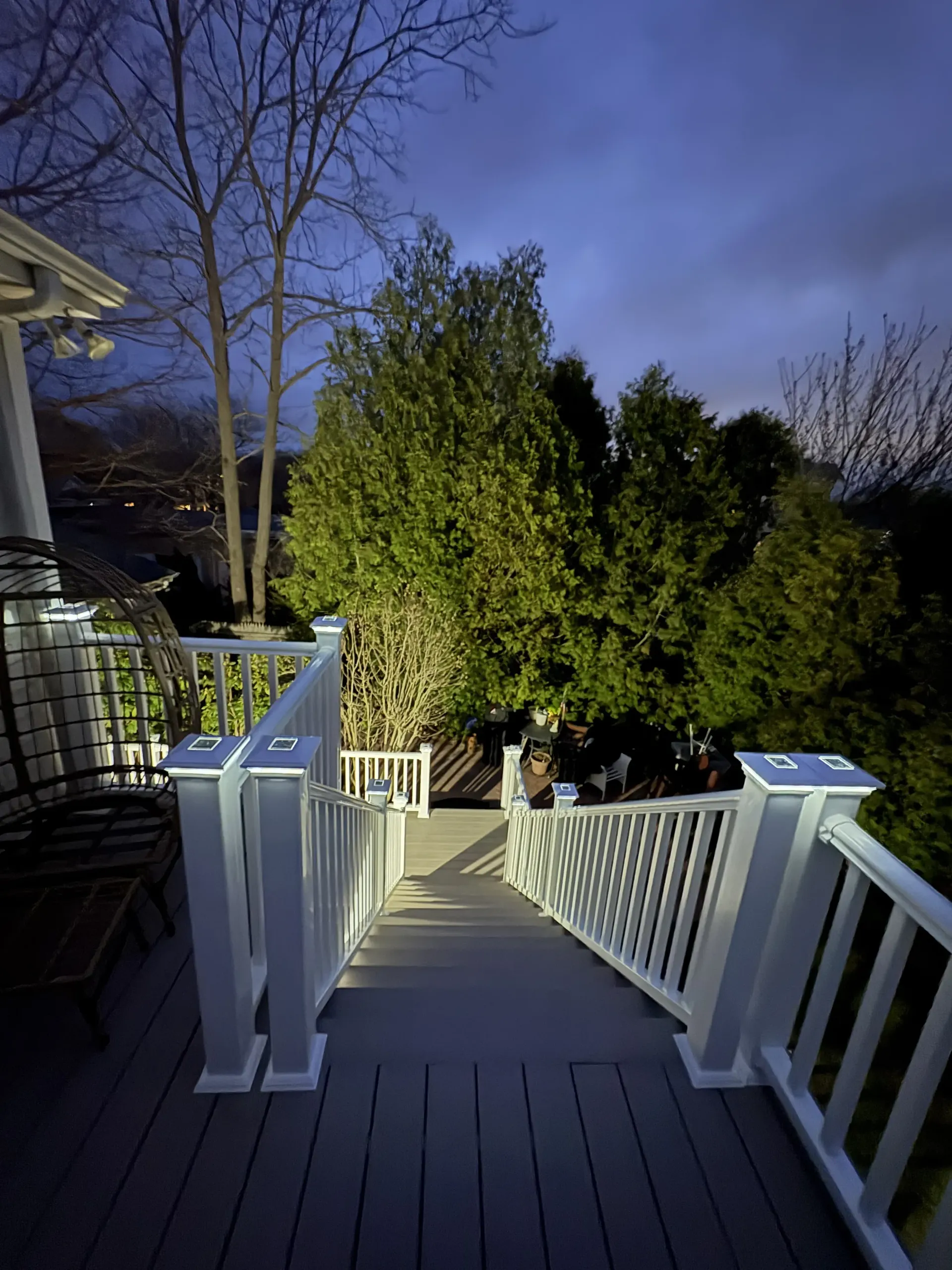Wooden deck stairs leading to a lit backyard with trees at dusk
