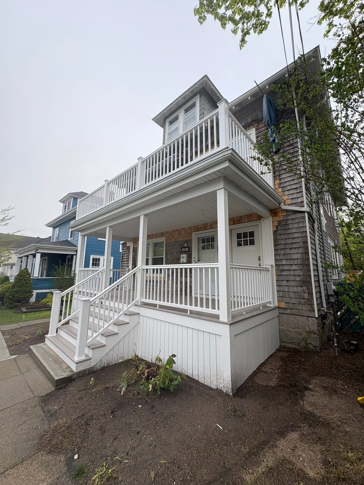 White two-story house with front porch, balcony, and stone siding on an overcast day