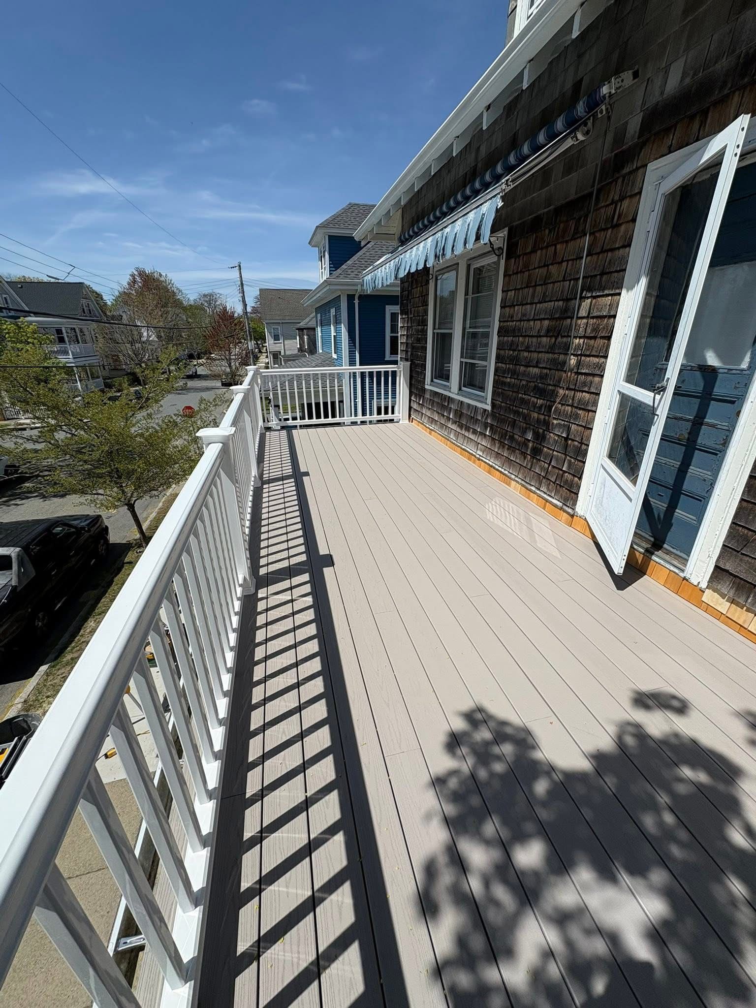 Sunlit apartment balcony with white railing, gray floor, and stone exterior wall under blue sky