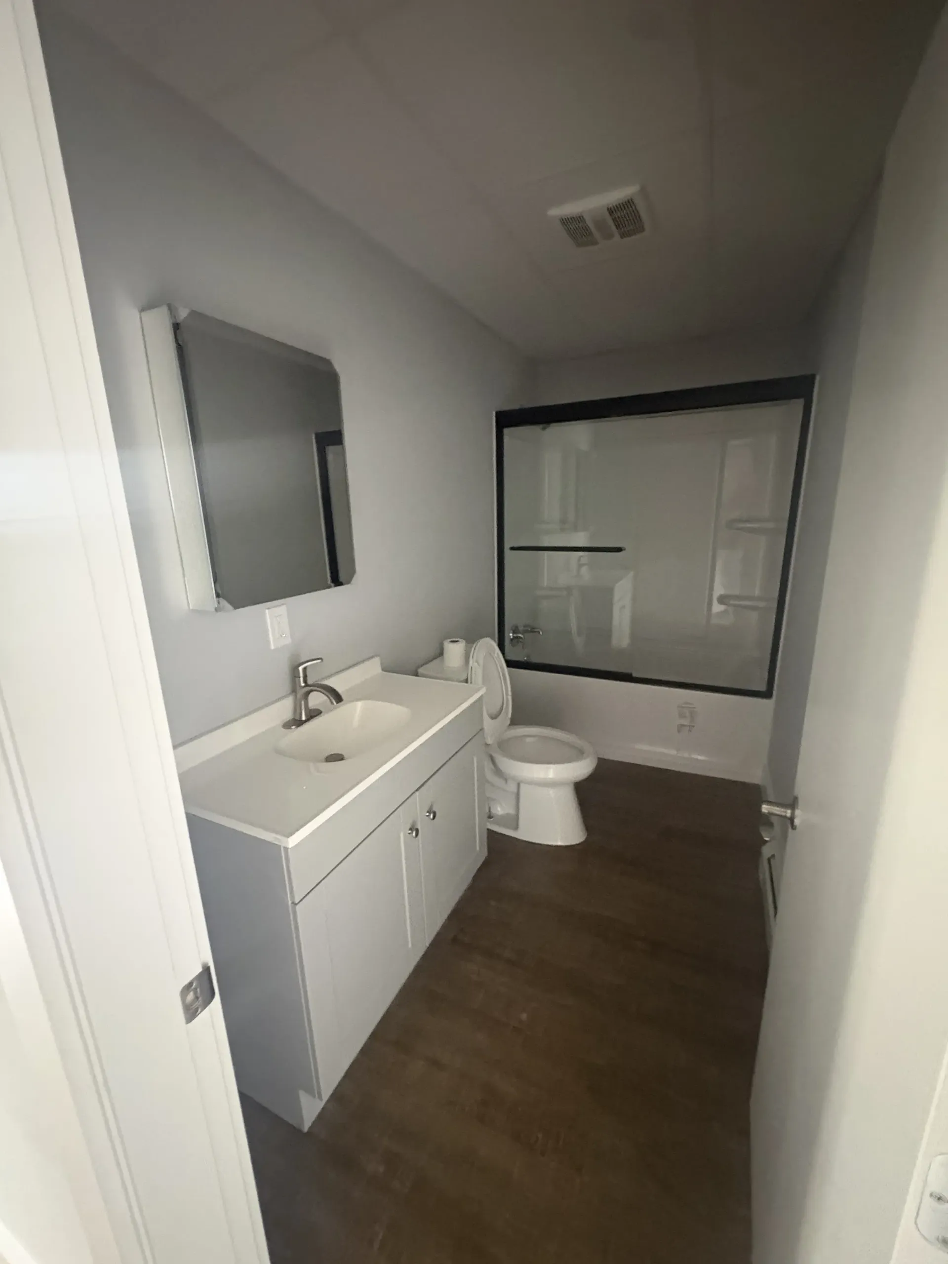 Small modern bathroom with white vanity, toilet, shower, and dark wood floor.