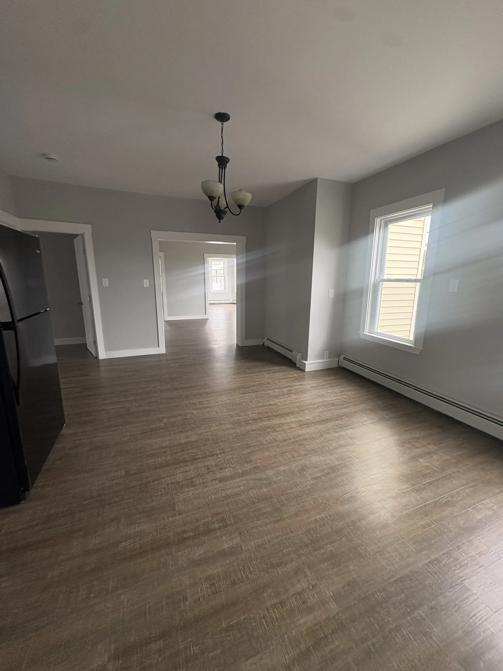 Empty living room with wood floors, gray walls, a chandelier, and bright windows.