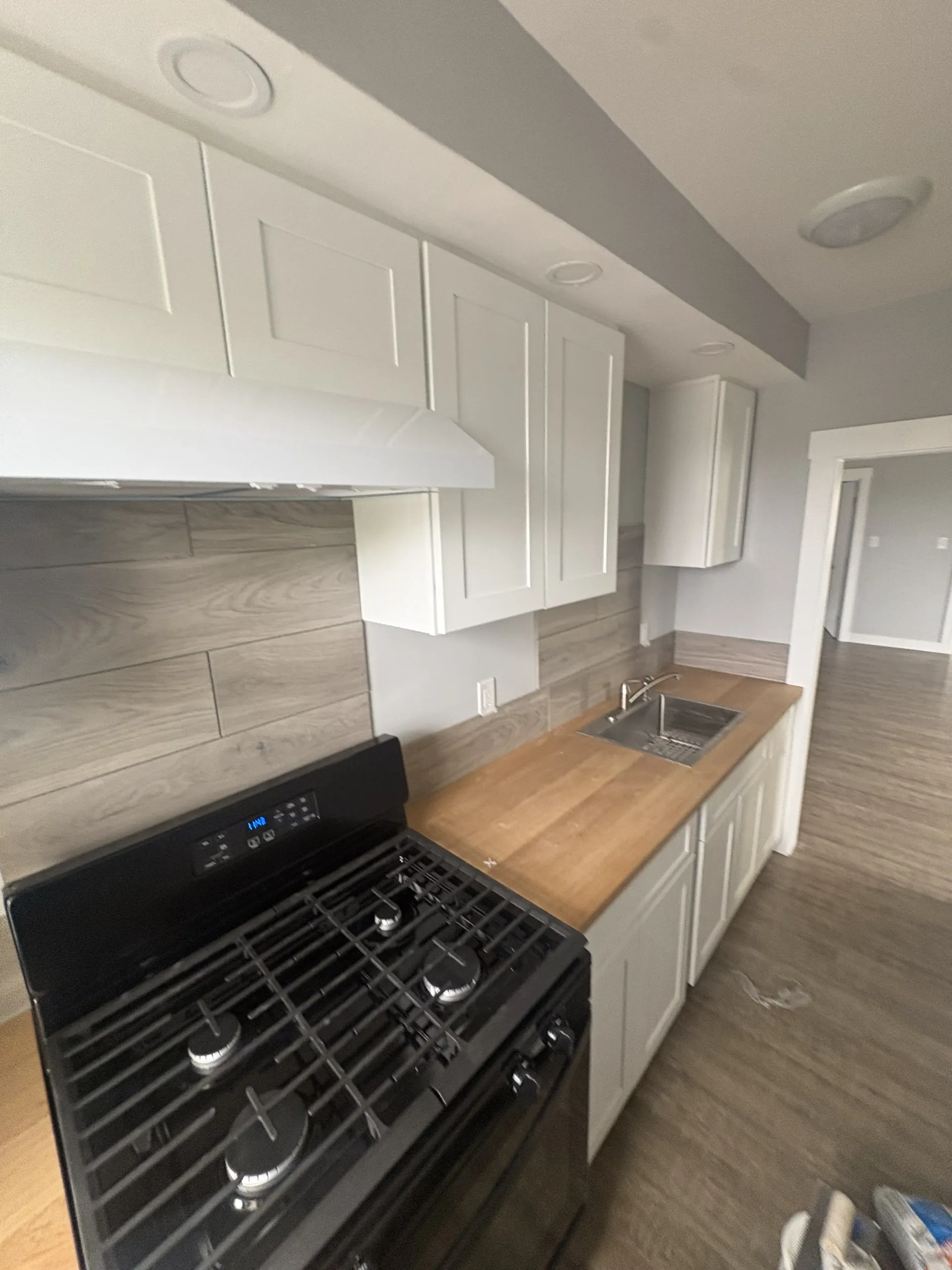 Modern kitchen with black gas stove, white cabinets, wood countertops, and stainless sink