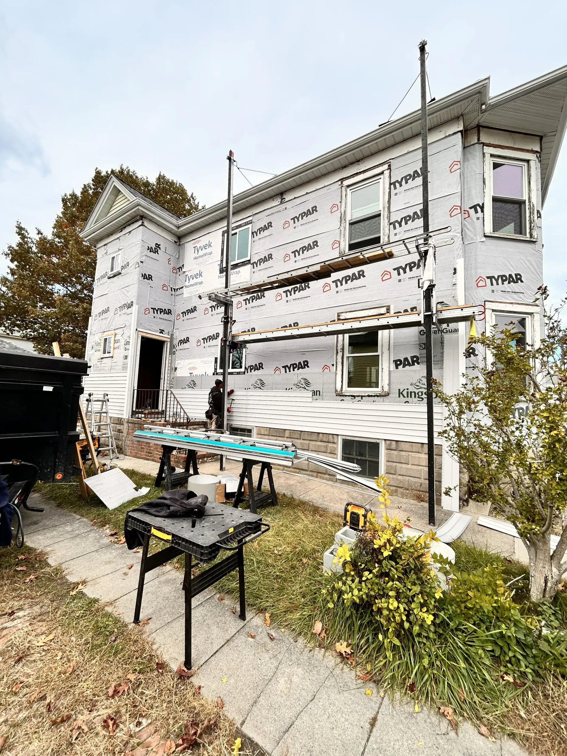 Two-story white house under construction with scaffolding and tools in the front yard