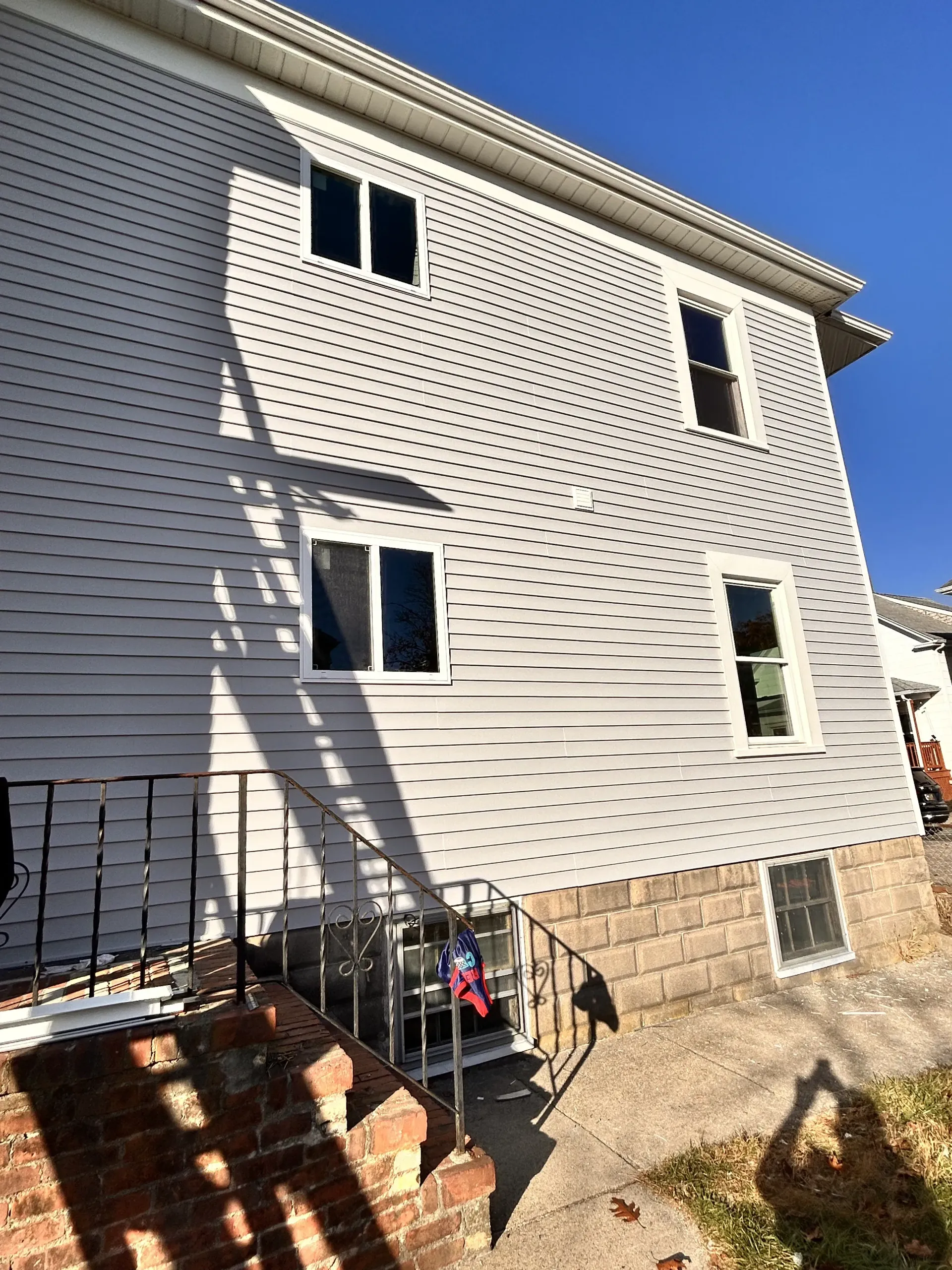 White vinyl house exterior with windows and a small front stoop with black railing, in bright sunlight.