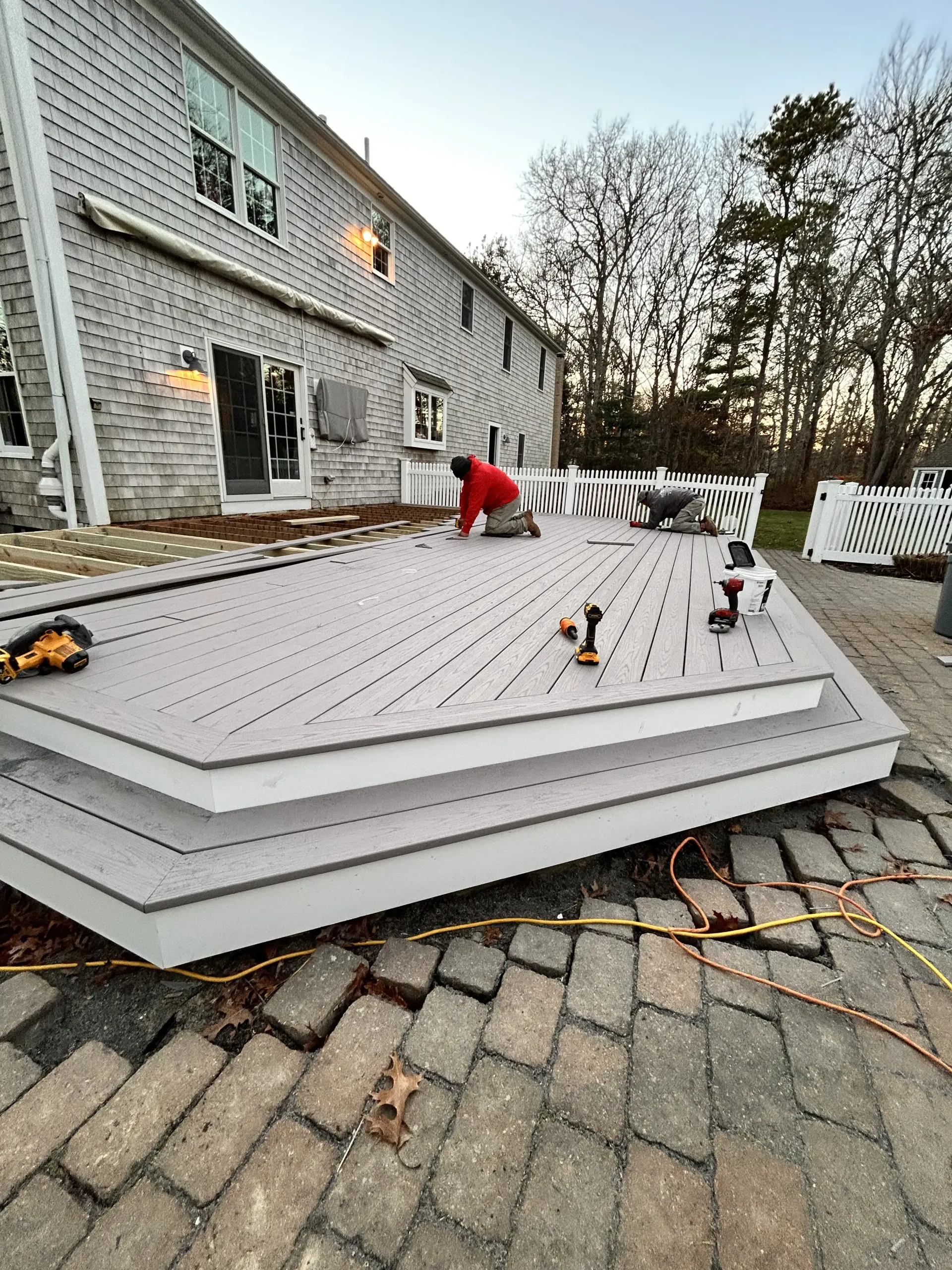 Stacked white foam boards and tools on a driveway beside a stone house at dusk.
