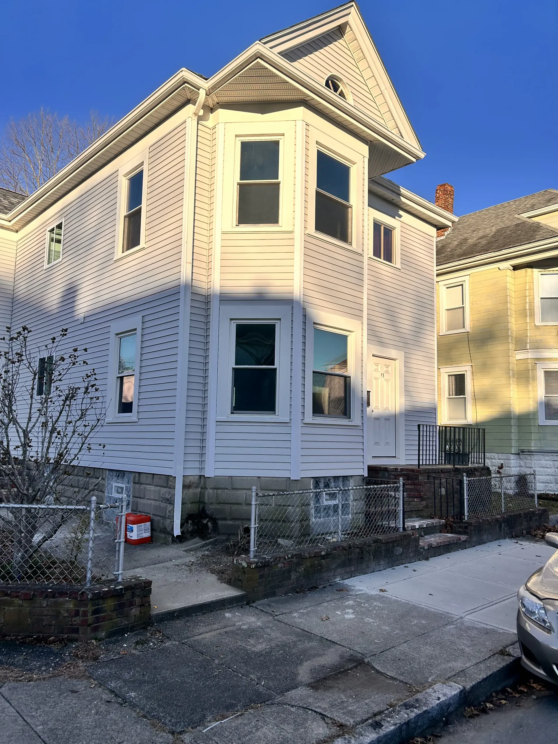 Two-story cream house with bay windows and a small front stoop on a residential street