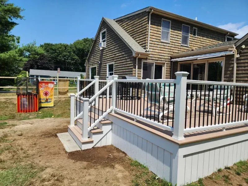 Raised wooden deck with white railings beside a house, in a sunny backyard