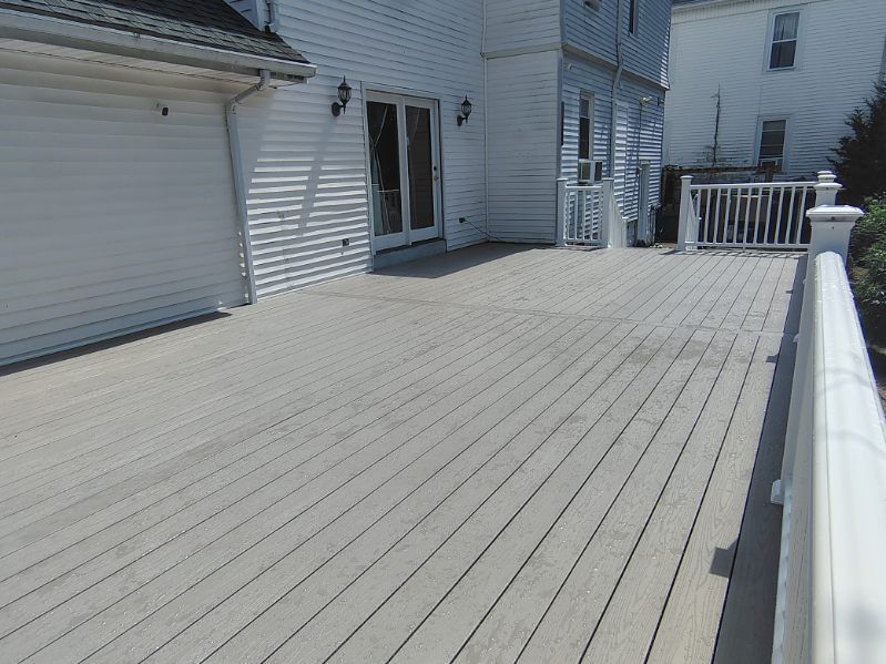 Empty white wooden deck beside a house, with railings and garage door in bright sunlight