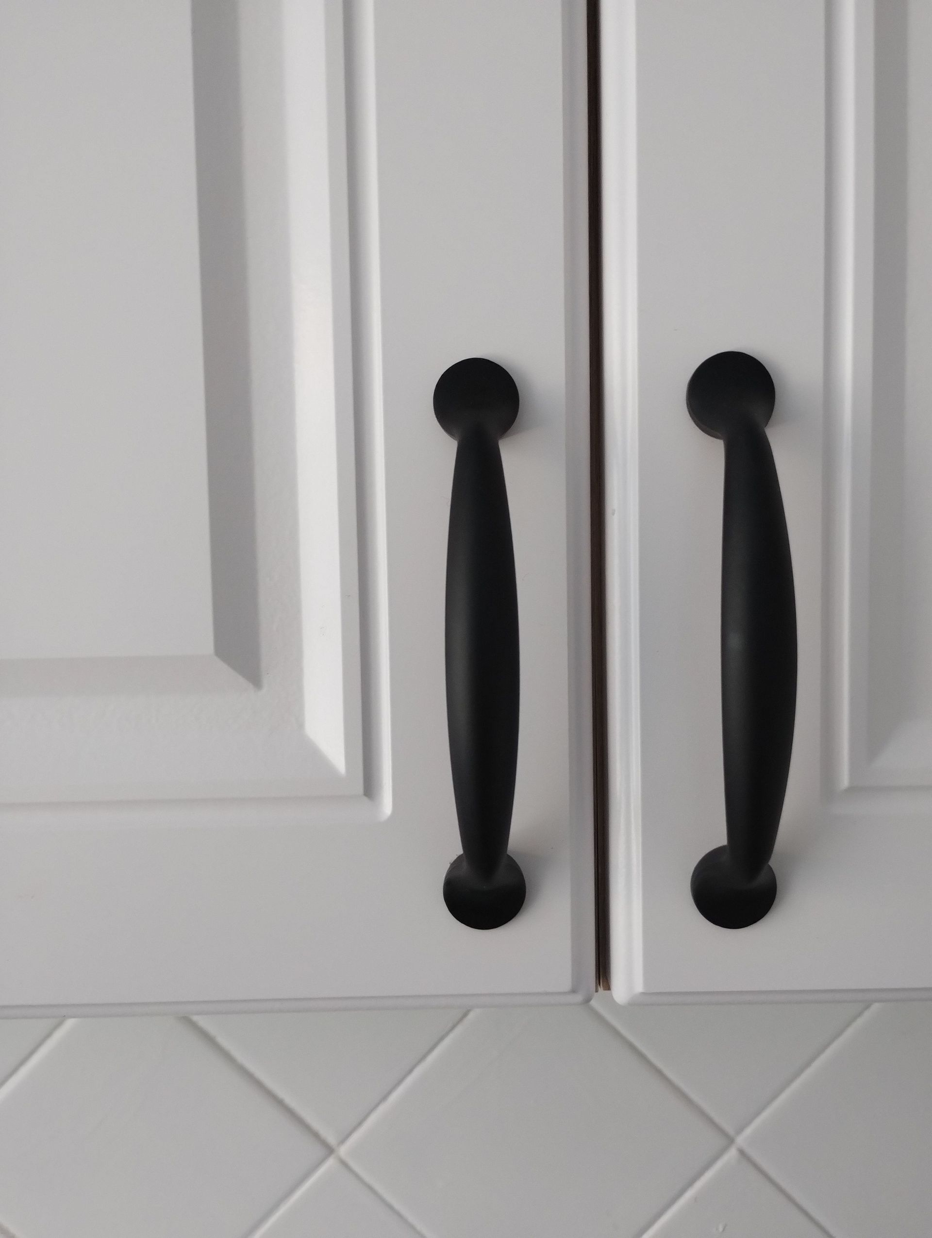 Close-up of white cabinet doors with black curved handles and a diamond-tile backsplash.