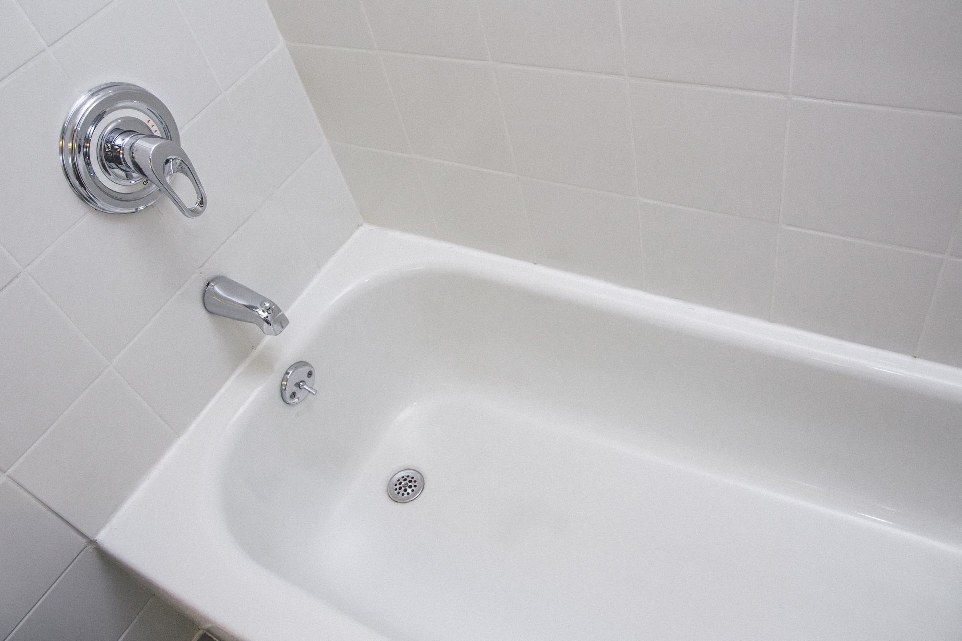 White bathtub with chrome faucet and shower controls in a tiled bathroom.