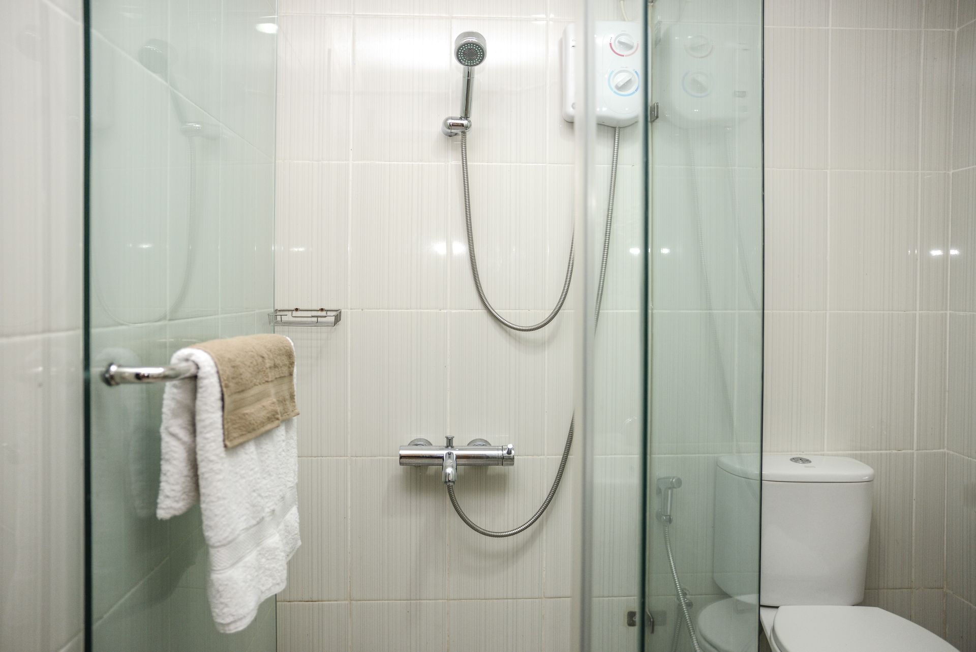 Modern shower with glass doors, white tile walls, and a towel on a chrome bar