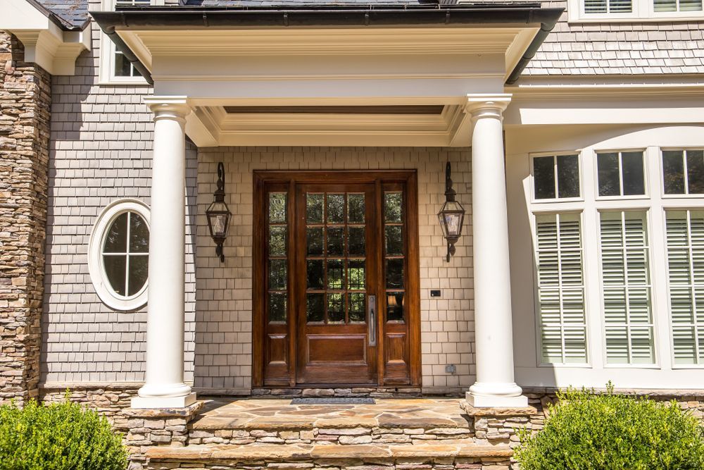 Front entrance of a house with white columns, stone façade, and wooden double doors