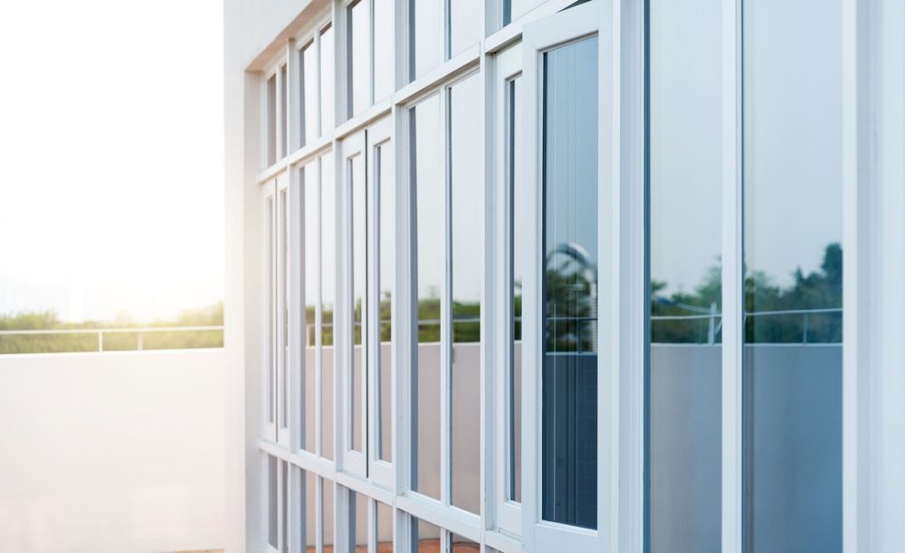 Modern glass building facade with tall white-framed windows in bright sunlight
