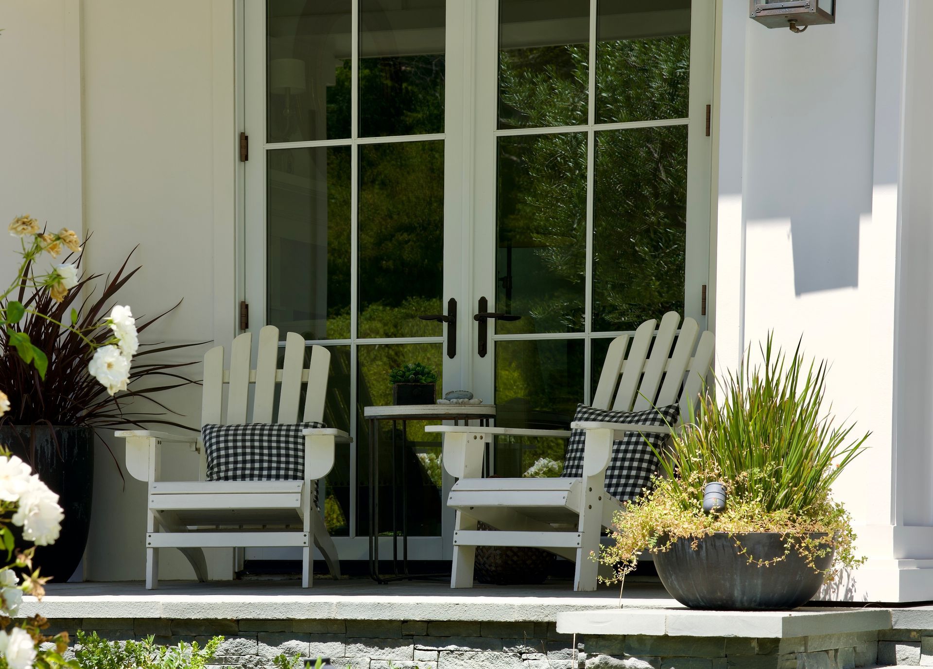 White porch with two Adirondack chairs, glass doors, and potted plants in front of a house
