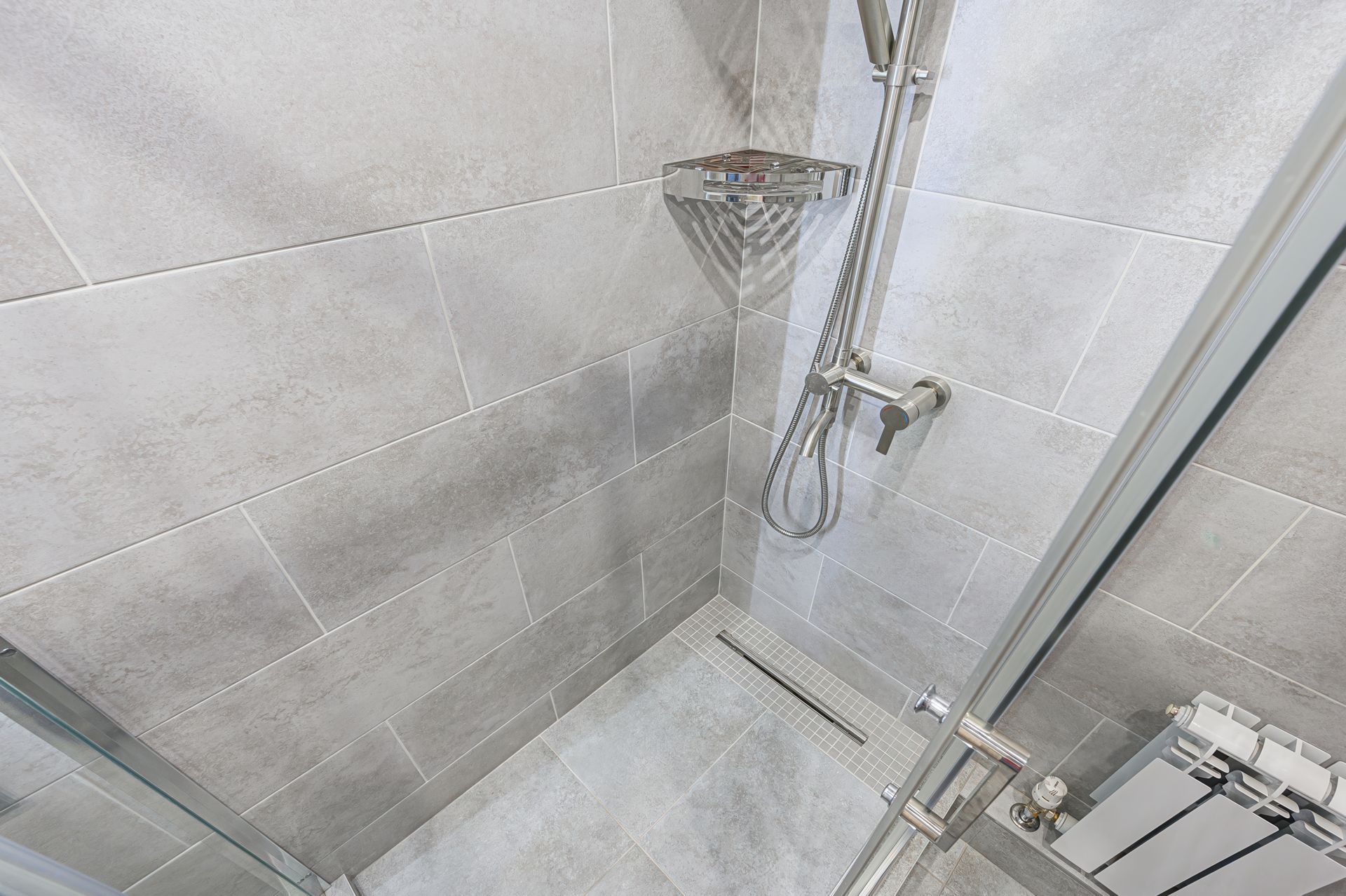 Tiled shower corner with a glass door, handheld showerhead, and chrome fixtures.