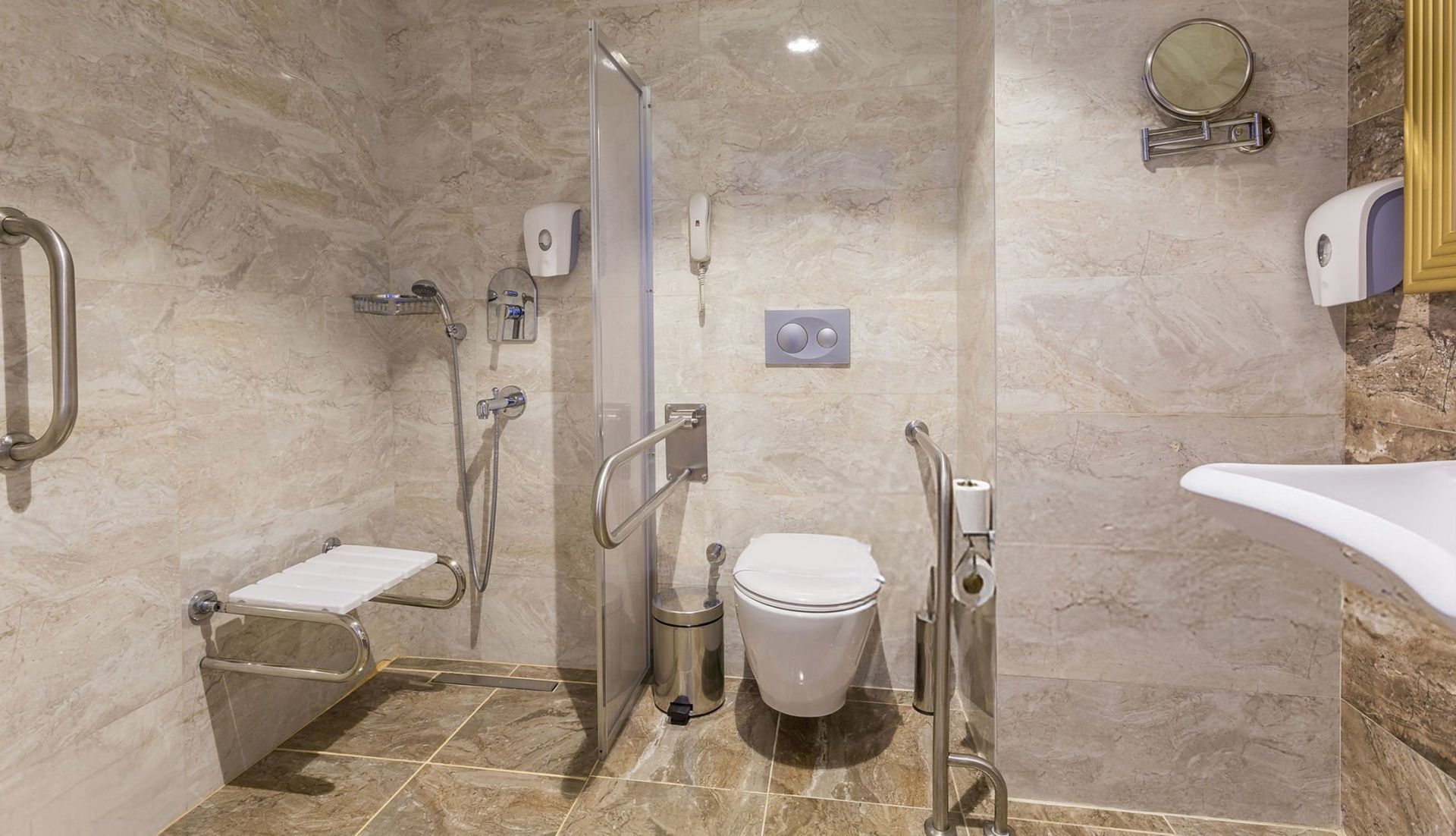 Accessible bathroom with marble tiles, toilet, grab bars, and a shower seat.