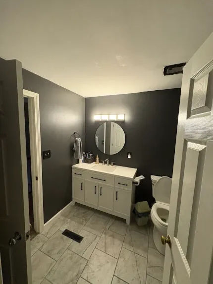 Bathroom with gray walls, white vanity, round mirror, bright vanity lights, and tiled floor