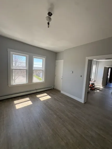 Empty gray room with wood-look floor, large window, and doorway to another room.