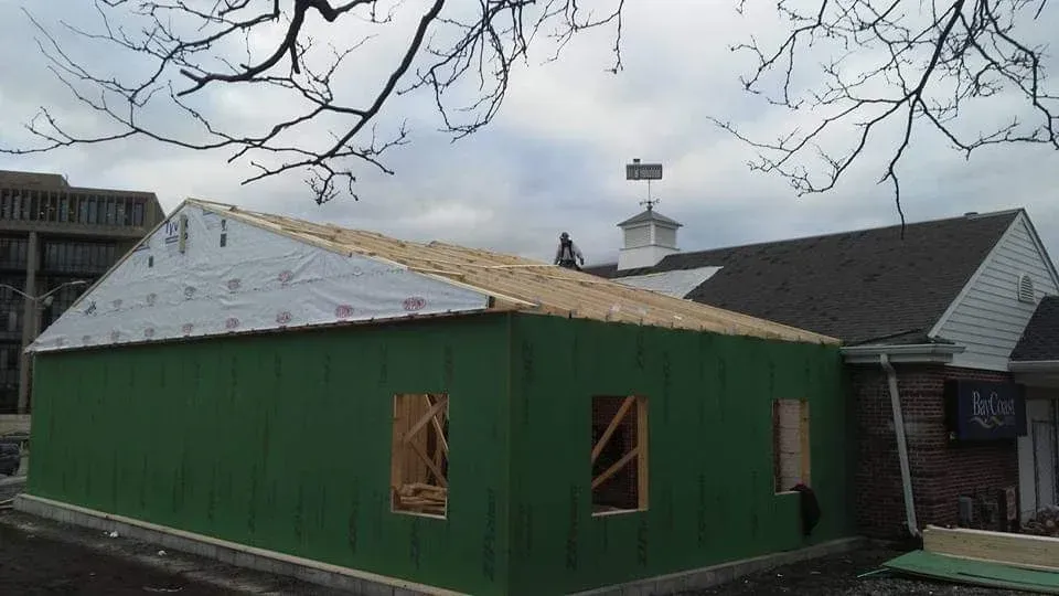Green-sided building under construction with white roof, viewed from outside on a cloudy day