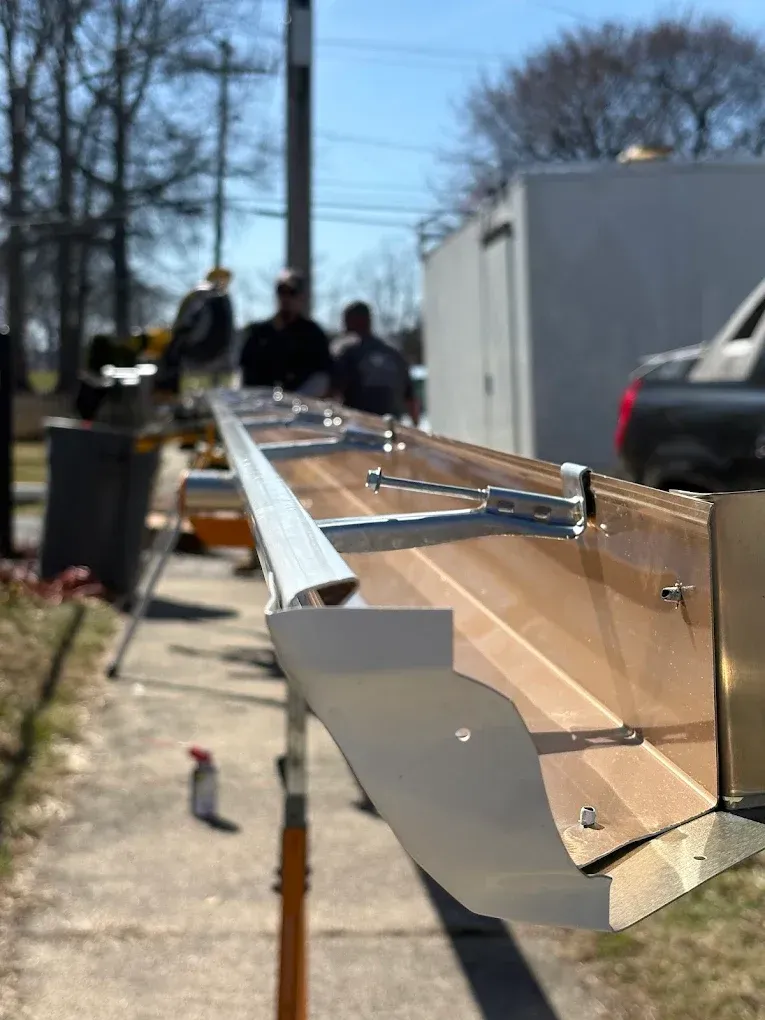 Close-up of a gutter guard on a rooftop, with workers and a truck blurred in the background.
