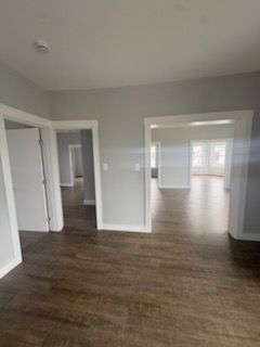 Empty gray room with dark wood floors, white trim, and open doorways to adjoining rooms