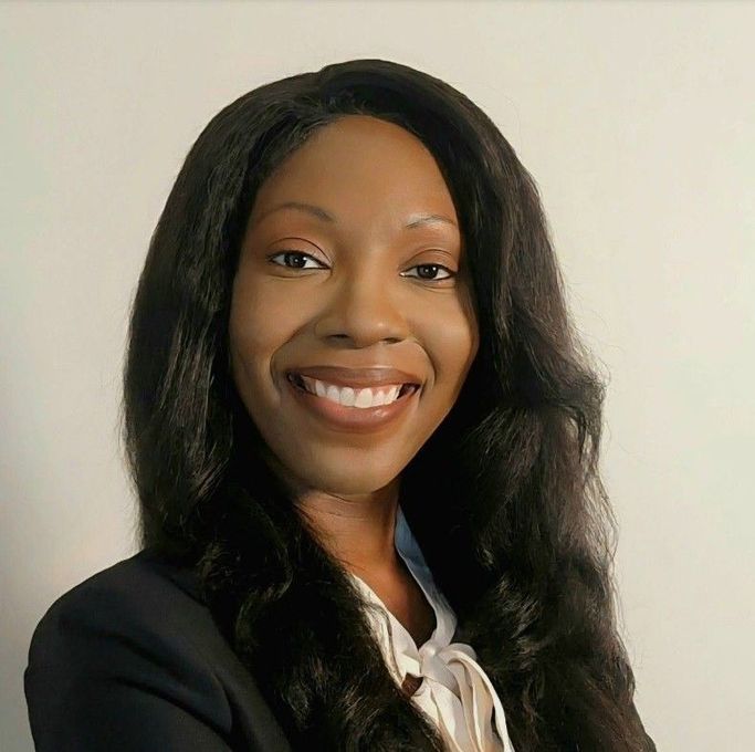 Smiling woman in a black blazer and white blouse against a light background