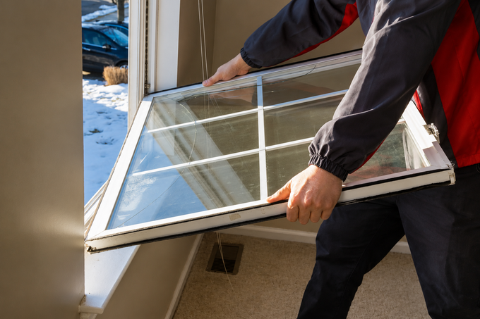Person carrying a large window frame indoors through a doorway