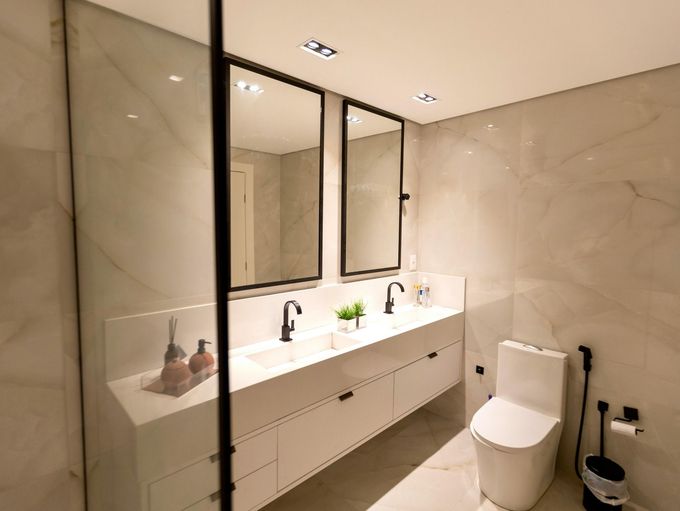 Modern minimalist bathroom with double sinks, black-framed mirrors, and a toilet beside a bidet sprayer.