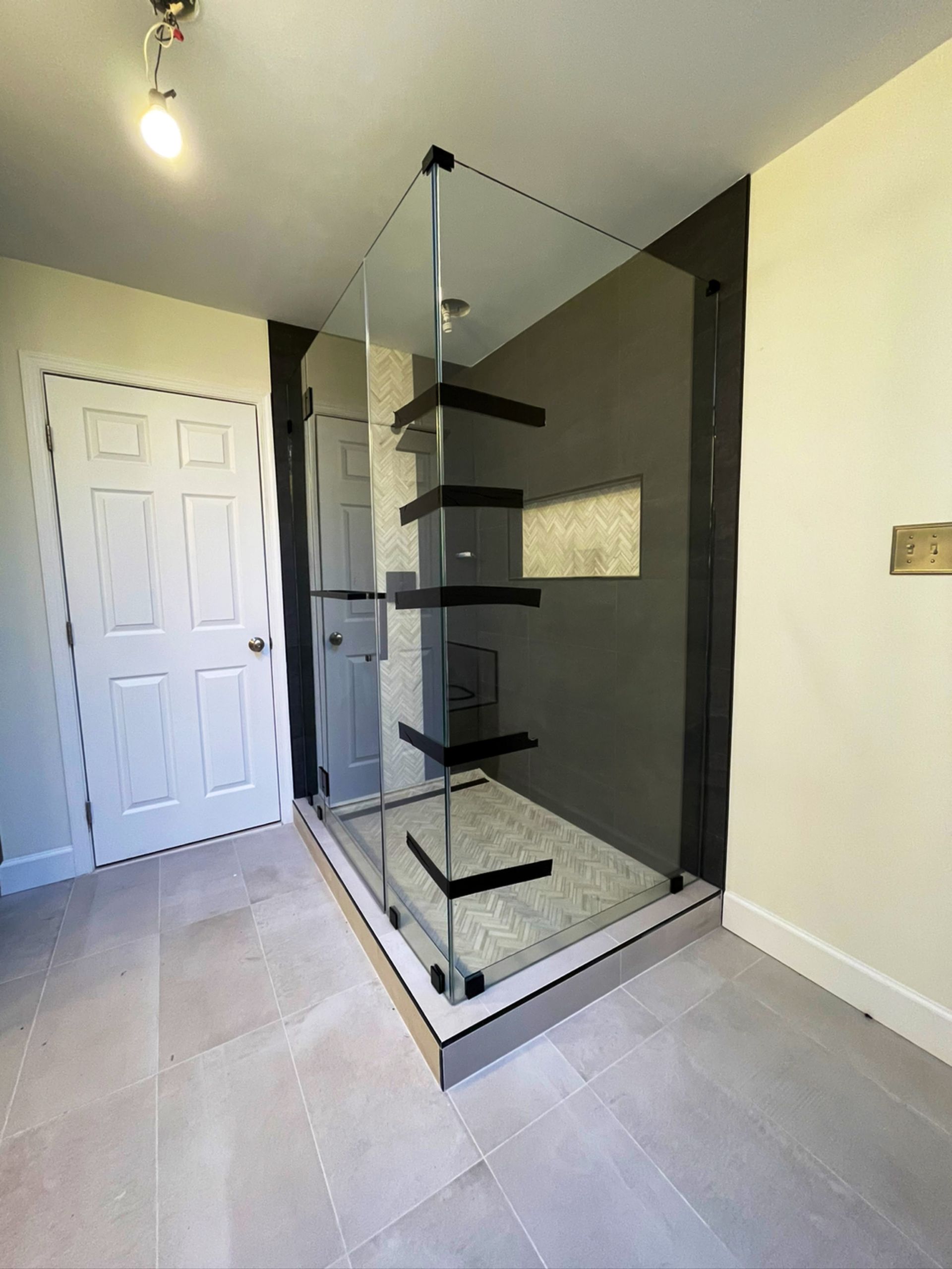 Modern glass shower enclosure with black shelves in a tiled bathroom room