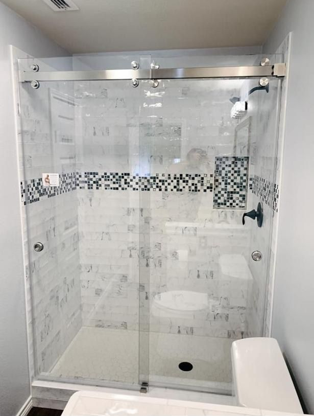 Modern glass shower with sliding door, gray tile accents, and a white bench seat