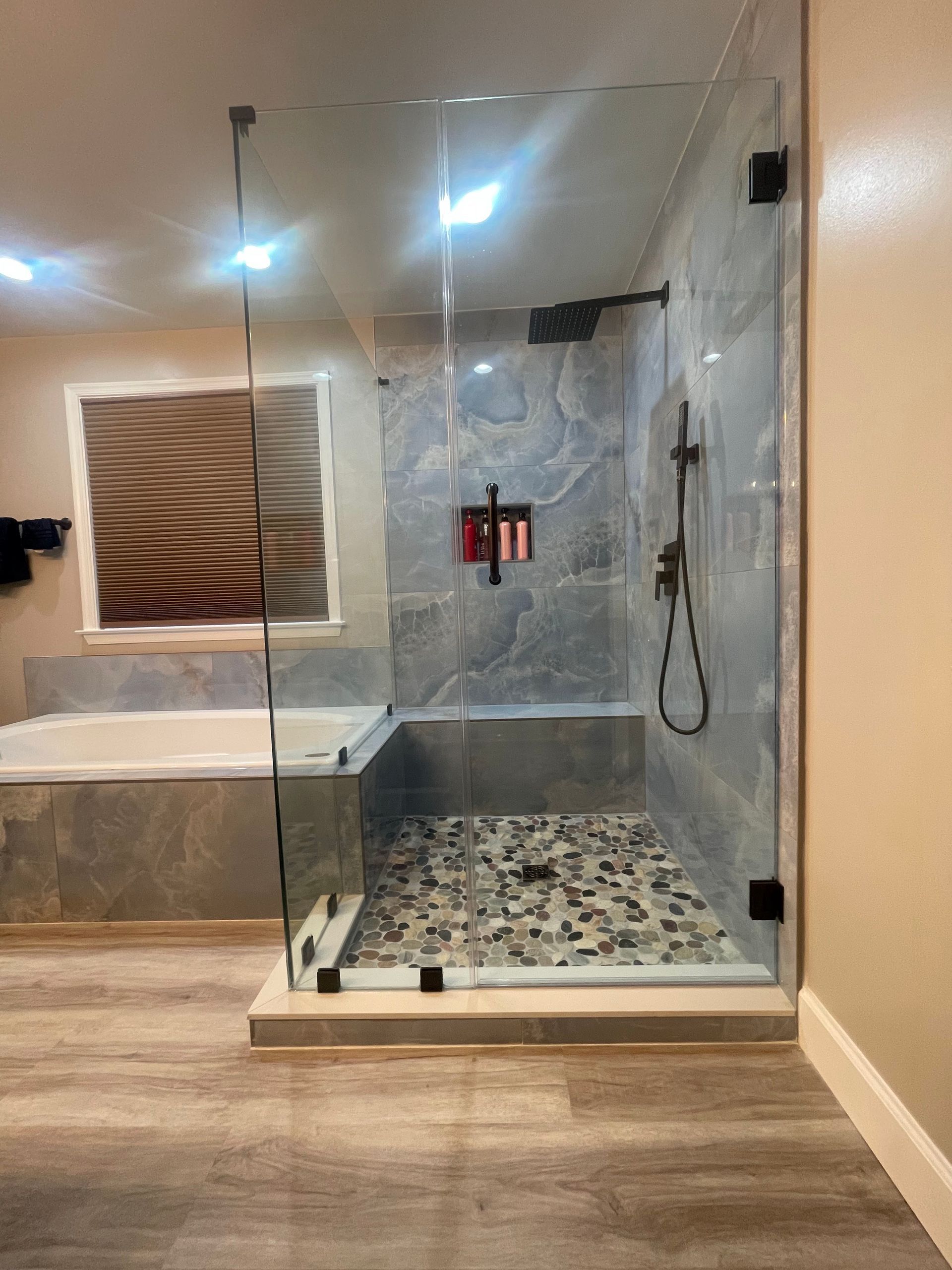 Modern glass shower with pebble-tile floor, marble walls, built-in shelf, and handheld showerhead