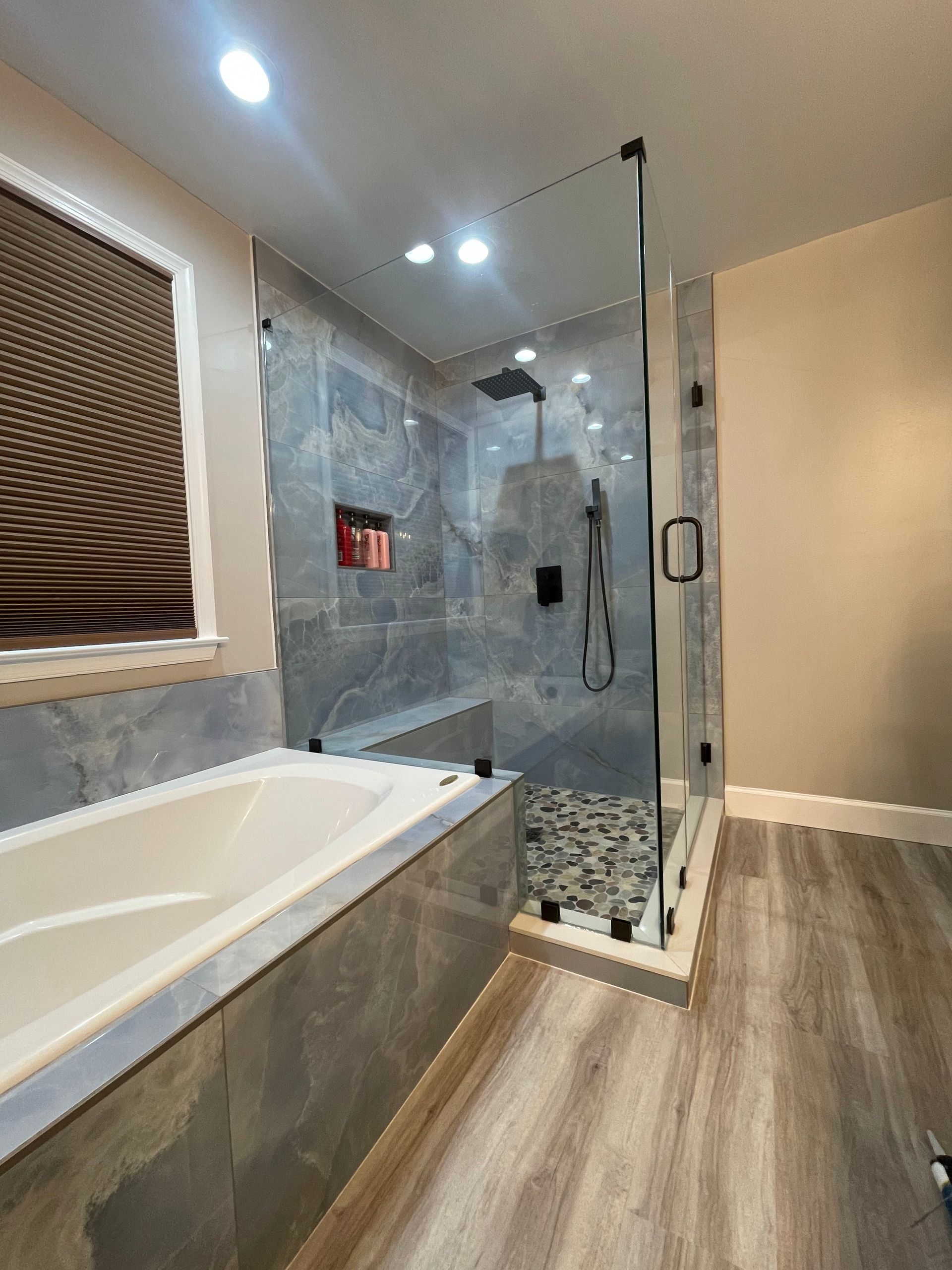 Modern bathroom with freestanding tub, glass shower, gray tile, and wood-look floor