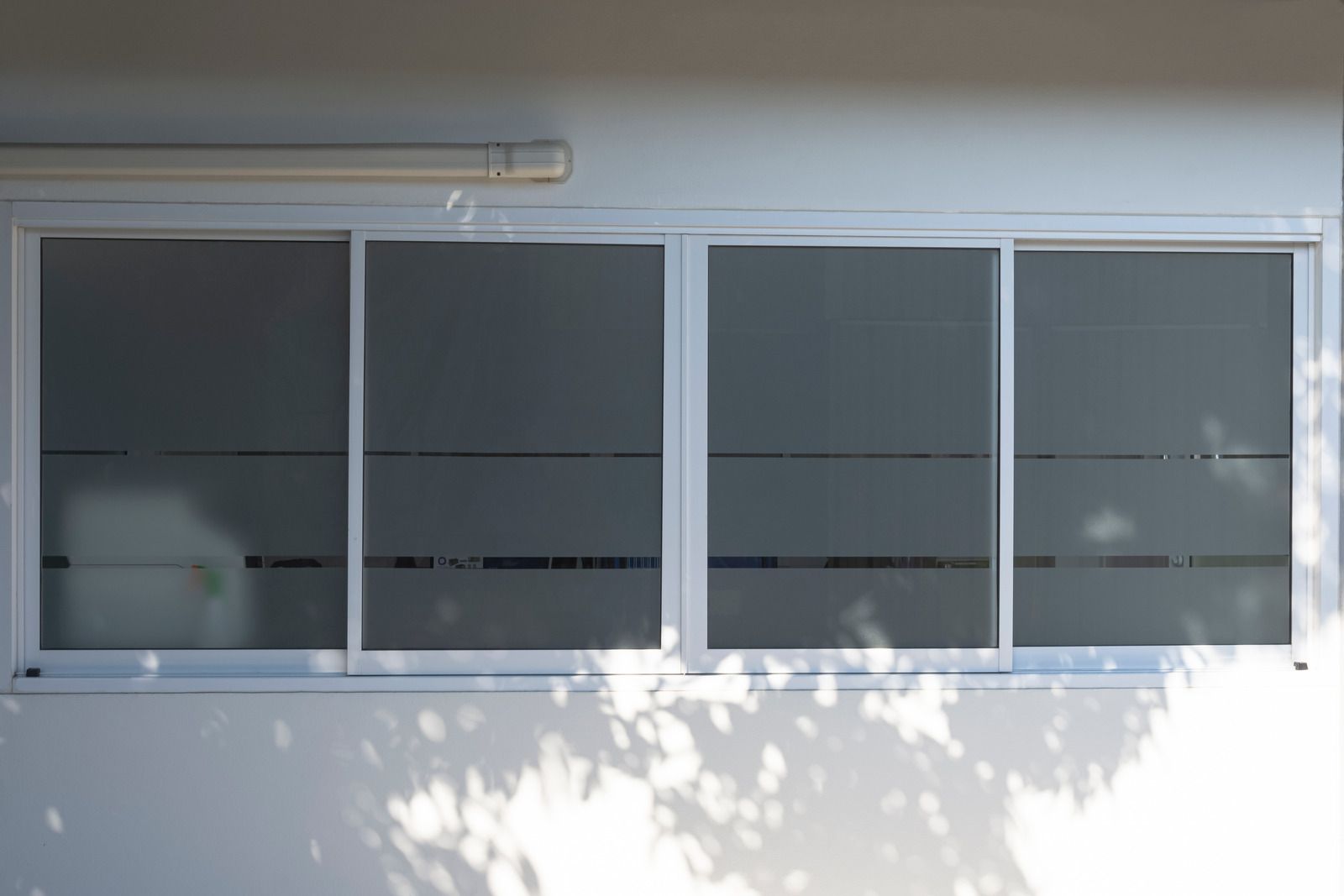 White building exterior with large sliding windows and tree shadows on the wall