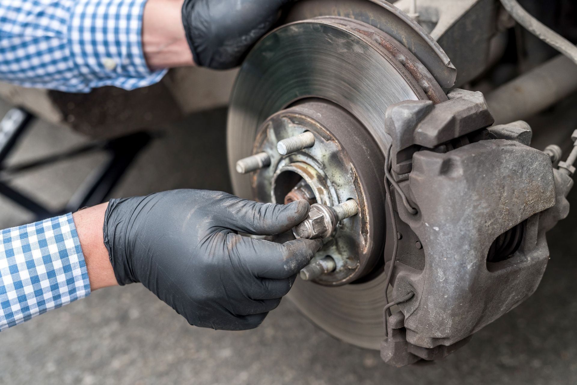 Mechanic’s gloved hands remove a car wheel hub and brake rotor during brake repair