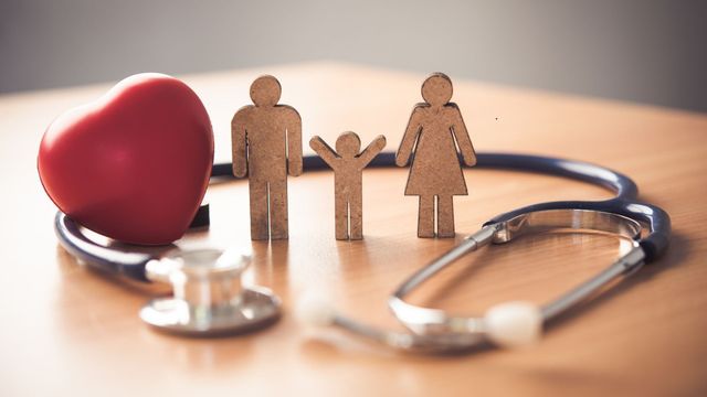 Family figurines, red heart, and stethoscope on a wooden surface, symbolizing health and care.