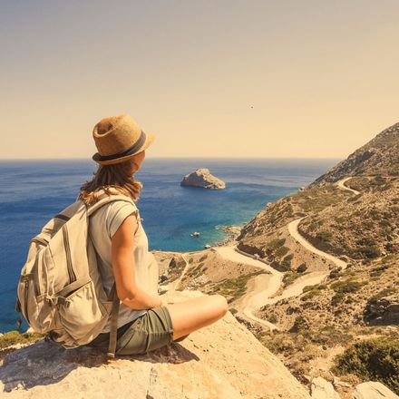 Woman in hat with backpack overlooking a winding road, ocean, and small island.