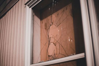 Cracked windowpane in a white frame with a broken blind behind it